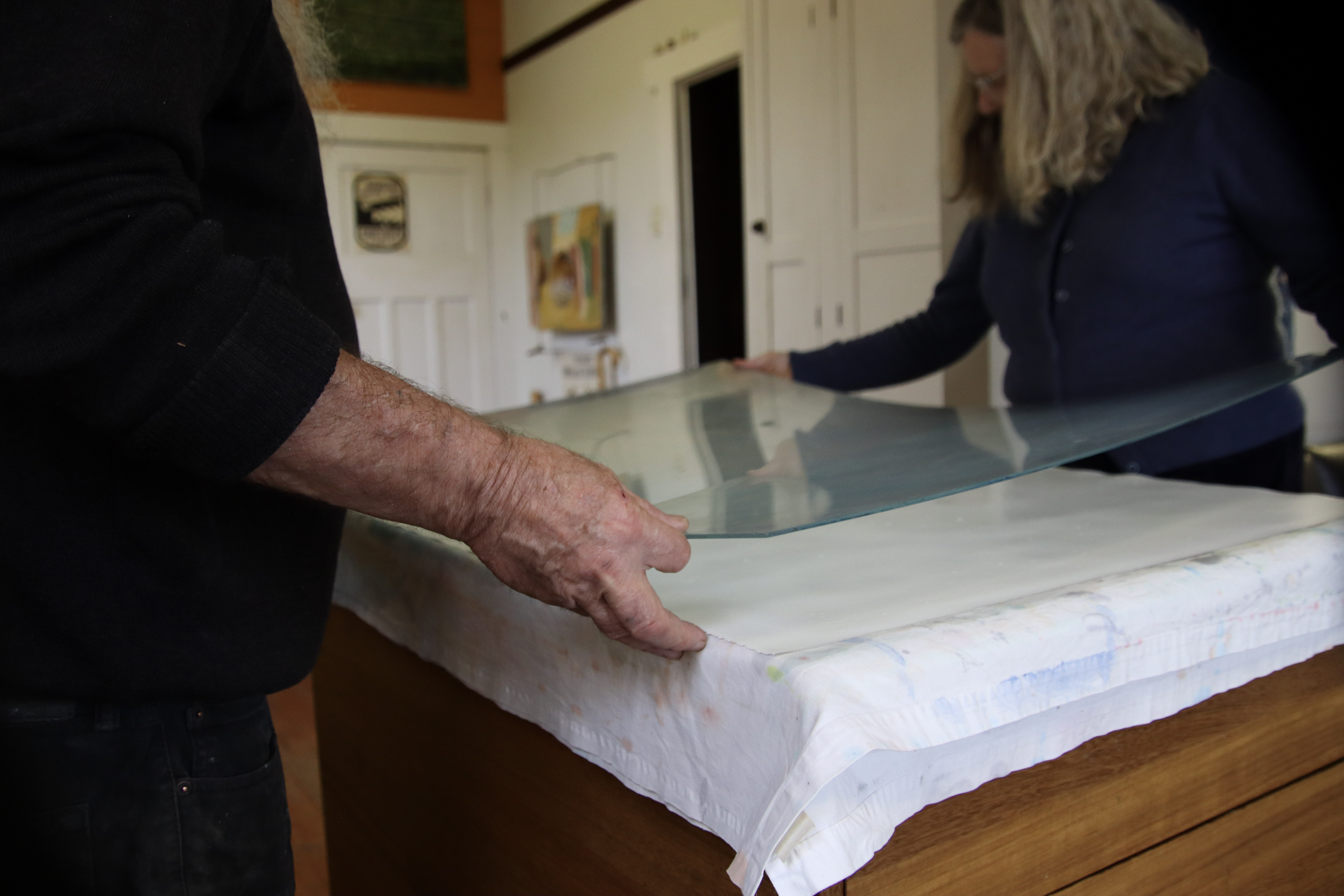 Image: paper preparation—acetate sheet being lowered on to wet paper. 