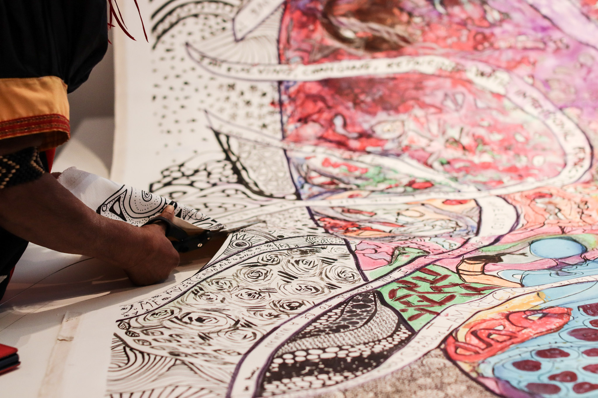 A person cuts into a large fabric, painted and drawn by IWD 2025 participants