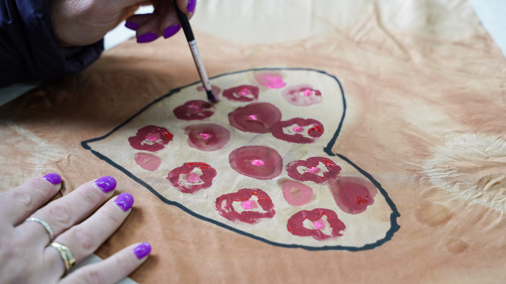 A workshop participant paints a patterned heart on a tie-dyed fabric.