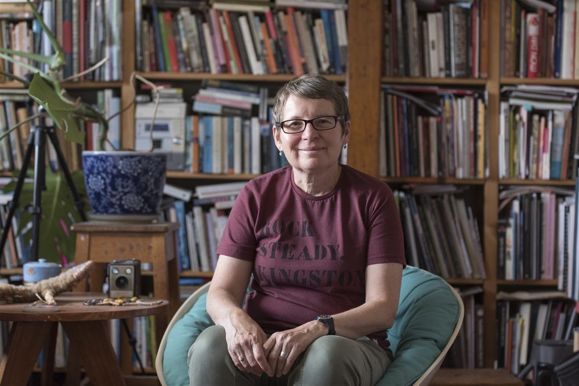 Woman (Julie Gough) sitting in front of book case