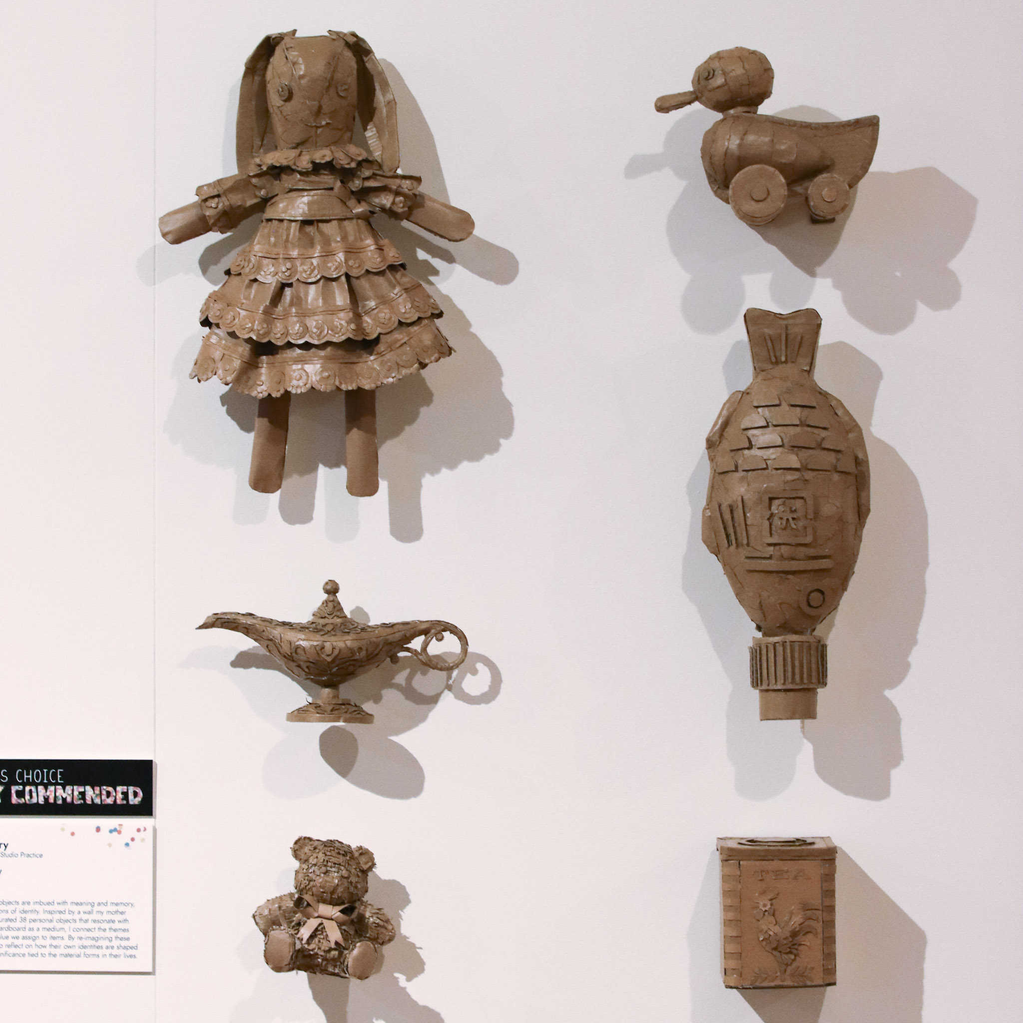 Echoes of Identity by Severine Cherry, 6 artworks made of cardboard and glue, resembling a doll, a toy duck, an oil lamp, an ornamental fish, a teddy bear, and a tea chest.
