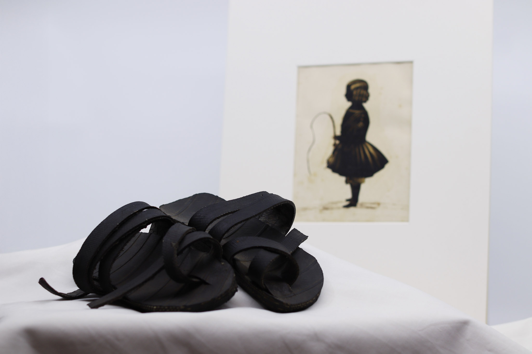 A pairing of objects from the Conversations exhibition - a pair of child's sandals and a painting of a girl with a riding whip in silhouette.