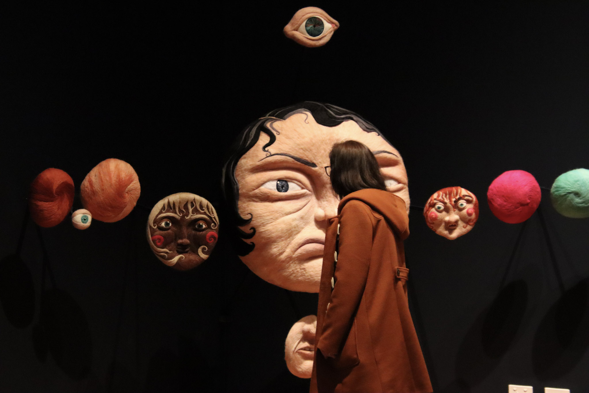 Woman standing in front of large scale needle felting faces by Tasmanian artist Frances Reeve Palmer in the exhibition RISE at QVMAG