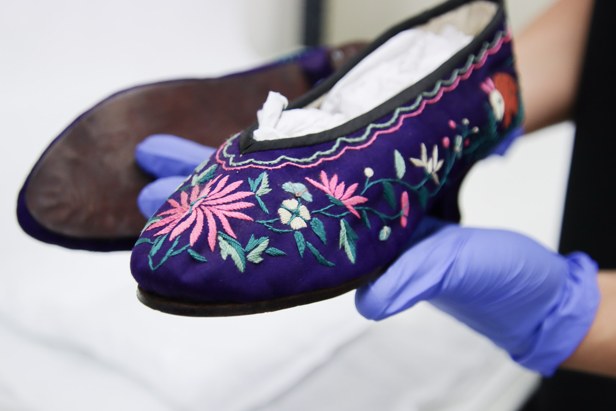 QVMAG curator demonstrates the embroidery on Ann Chung Gon's shoes